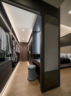 a walk in closet next to a bed and dressing table with clothes on hangers