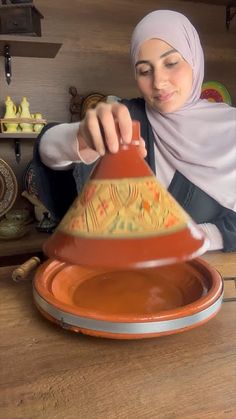 a woman is sitting at a table making something out of an orange bowl and saucer