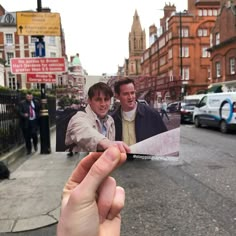 a hand holding up a photo of two men on the street in front of some buildings