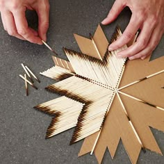 two hands are working on an ornament made out of matches and wood sticks