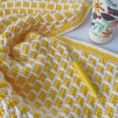 a crocheted blanket next to a cup and pen