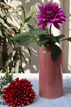 a pink vase with purple flowers in it next to a red flower