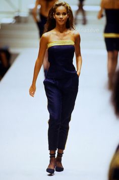 a model walks down the runway in a strapless blue and yellow top with black pants