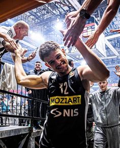 a group of men standing next to each other on top of a basketball court with their hands in the air