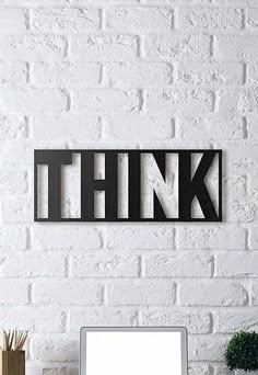 a laptop computer sitting on top of a desk next to a white brick wall with the word think above it