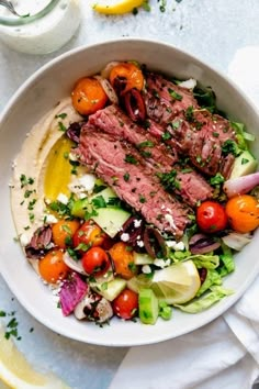 a white bowl filled with meat, tomatoes and cucumber on top of a table