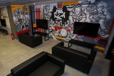 a room with couches, chairs and televisions in front of graffiti on the wall