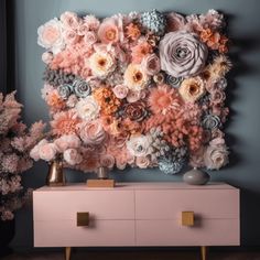 a pink dresser topped with lots of flowers next to a wall mounted flower art piece