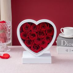 a heart shaped box filled with red roses next to a stack of books and a cup