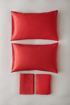 two red pillows and one orange pillow on a white surface