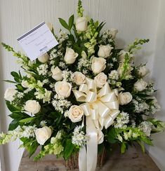 a bouquet of white roses and greenery in a basket with a note attached to it