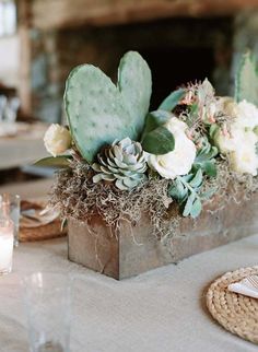 an arrangement of flowers and succulents in a metal container on a table