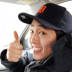 a woman wearing a baseball cap gives the thumbs up sign in a car with another person behind her