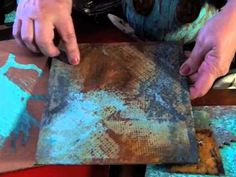 two hands are working on an old piece of paper with blue and brown paint over it