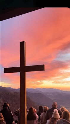 a group of people standing in front of a wooden cross at the top of a hill