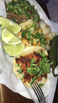 a plate filled with tacos and limes on top of a table