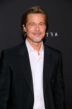 a man in a black suit and white shirt smiles at the camera while standing on a red carpet