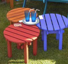 three colorful wooden tables and chairs in the grass with drinks on each table, including one for two