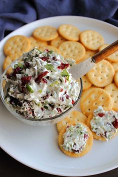 a white plate topped with crackers and a bowl of cranberry cream cheese spread