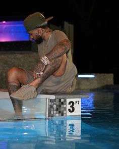 a man sitting on the edge of a swimming pool with his feet in the water