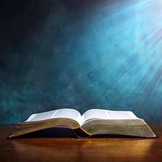 an open book sitting on top of a wooden table next to a blue wall with beams of light coming from it