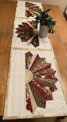 two quilted table runneres sitting on top of a wooden table next to a potted plant