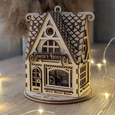 a small wooden house with lights around it on a table next to a potted plant