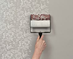 a person is using a paint roller to paint a wall with flowers and vines on it