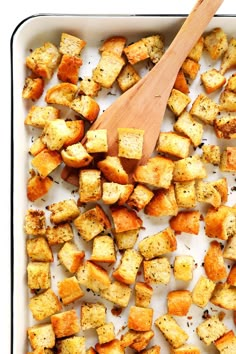 a wooden spoon is in a casserole dish full of bread cubes and potatoes