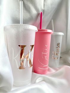 three different colored cups sitting on top of a white cloth covered bed next to each other