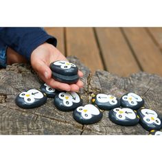 a hand holding a rock with penguins painted on it sitting on top of a tree stump