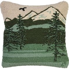 a green and white pillow with trees on the front, birds flying in the background