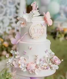 a three tiered wedding cake with flowers and butterflies on the top is decorated in pastel colors