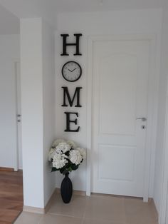 a black vase with white flowers in front of a sign that says home on the wall