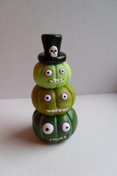 a stack of three green halloween pumpkins with googly eyes and a top hat