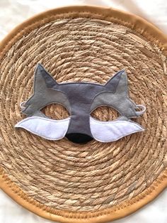 a close up of a cat mask on a woven place mat with white and gray accents