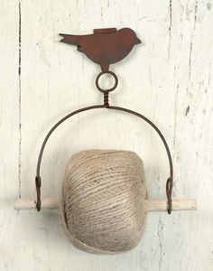 a ball of yarn is hanging from a hook on a white wooden wall with a bird