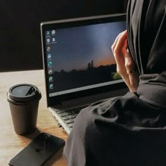 a person sitting in front of a laptop computer on a wooden table next to a cup of coffee