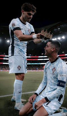 two soccer players are sitting on the ground and one is holding a crown while the other looks at him