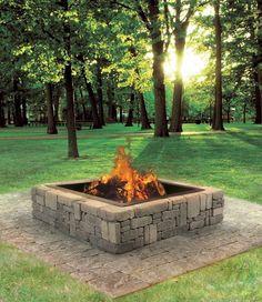 a fire pit sitting in the middle of a park with trees and grass behind it