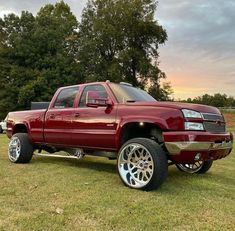 a red truck parked on top of a grass covered field with trees in the background