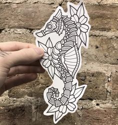 a hand holding up a sticker with an image of a sea horse on it