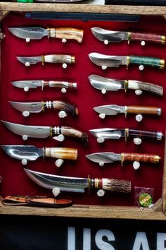 an assortment of knives are displayed in a wooden box with red velvet lining the bottom