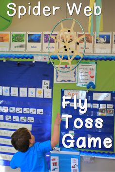 a young boy is playing with a spider web in front of a classroom bulletin board