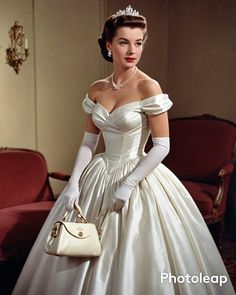 a woman in a white dress and tiara is holding a handbag while standing next to a red couch