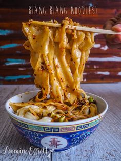 someone holding chopsticks over noodles in a blue and white bowl with the words bing bang noodles on it