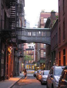 a woman is walking down the street under an overpass with fire escapes on it