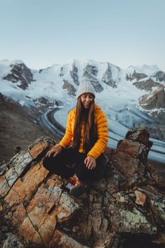 a woman sitting on top of a mountain with snow covered mountains in the back ground