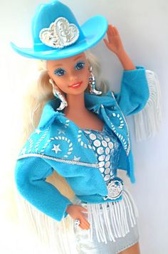 a barbie doll wearing a blue cowboy hat and fringed skirt with her hand on her hip