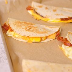 three quesadillas sitting on top of a brown paper lined baking pan with eggs and bacon